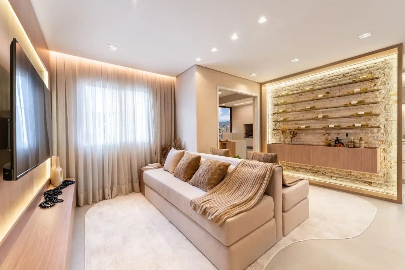Sala de estar com sofá bege, painel para TV e estante iluminada