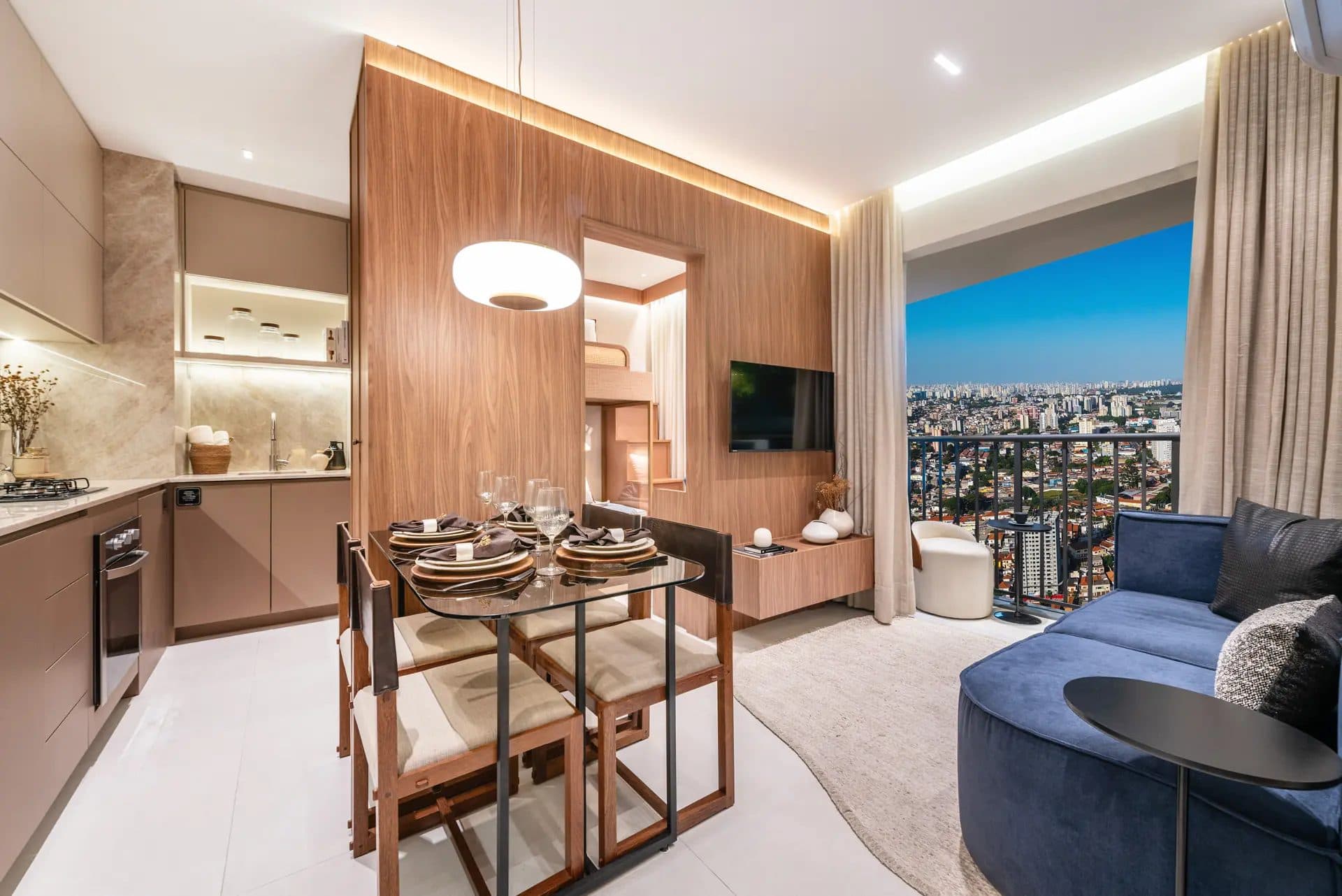 Sala de estar e jantar integrada com mesa de vidro, sofá azul e acesso à varanda com vista panorâmica.